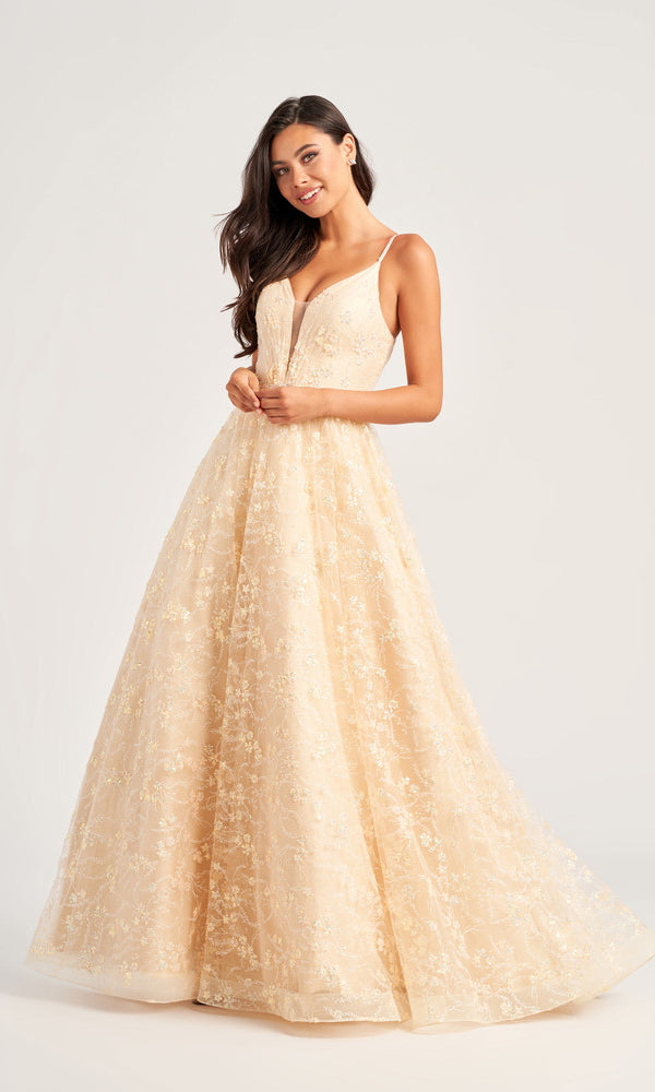 A woman poses against a plain light background wearing the Glitter-Tulle Colette Long Prom Ball Gown CL5288, a sleeveless, floor-length light beige dress with a deep V-neck, floral embroidery, beaded waist, and glitter-tulle fabric.